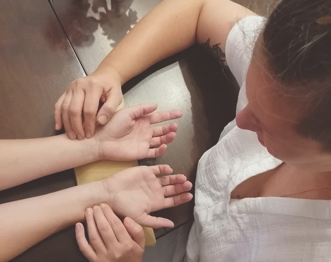 Fotografie von oben: eine Person hat ihre Finger auf den Pulstaststellen am Handgelenk einer anderen Person. Es sind jeweils beide Hände sichtbar.
