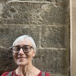 Foto von einer lächelnden grauhaarigen Frau vor einer Wand