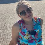 Foto einer lächelnden Frau mit Sonnenbrille und buntem Oberteil